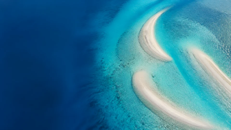 Cobalt depth opens into three impossible aquamarine sandbars and a vast submerged limestone shelf.