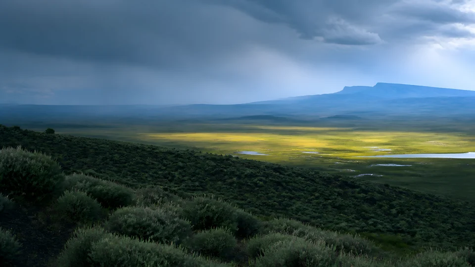 Sage, flood meadow, and volcanic weather form three quiet bands across an invented high-desert basin.