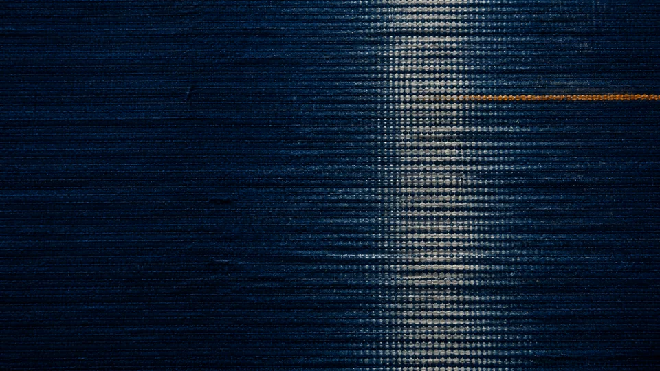 A pale resist interval and one saffron crossing hold their register inside a deep indigo warp.