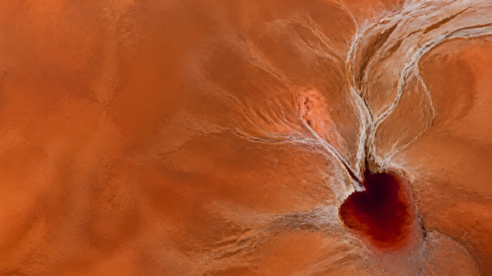 Pale dry channels converge on one oxblood remnant pool across a vast burnt-sienna basin.